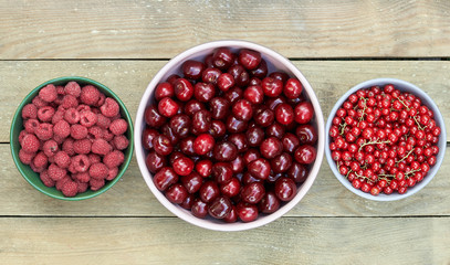 Bowls with fresh garden and forest red berries: raspberry, sweet cherries, red currant overhead flatlay on the wooden table, flat lay, from above top viiew, closeup, copy empty space for your design