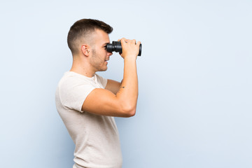 Young handsome blonde man over isolated blue background with black binoculars