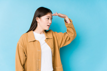 Young chinese woman posing in a blue background isolated looking far away keeping hand on forehead.