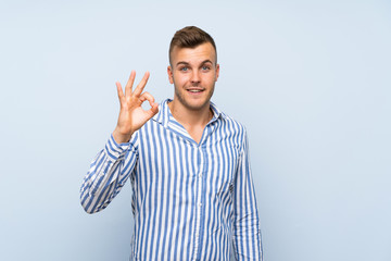 Young handsome blonde man over isolated blue background showing ok sign with fingers