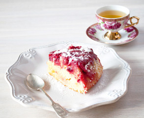 Piece of cranberry tart, pie, cake on plate, tea spoon, cup of tea on white wooden table backgound.