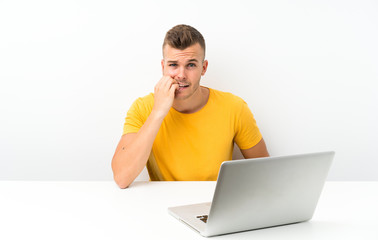 Young blonde man in a table with a laptop nervous and scared