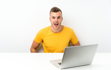 Young blonde man in a table with a laptop with surprise facial expression