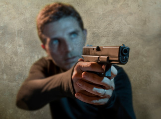 grunge cinematic portrait of attractive and dangerous looking hitman or secret service especial agent man in action pointing gun in crime mob and criminal lifestyle concept