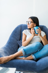 Young pretty woman sitting in armchair and drinking coffee at home