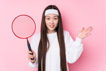 Young chinese woman playing badminton isolated receiving a pleasant surprise, excited and raising hands.