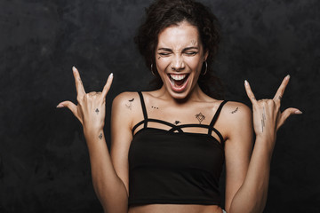 Image of young excited woman screaming and gesturing horns with fingers