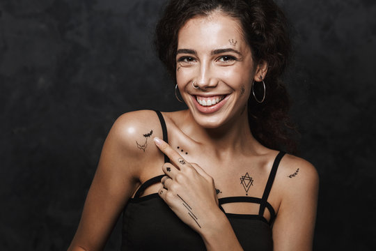 Image of beautiful happy woman smiling and pointing finger at her tattoo