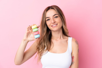 Young woman with  macarons over isolated pink background smiling a lot