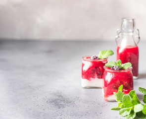 Glass jars of healthy layered berries and yogurt smoothie. Mix berry smoothie with raspberry, blackberry and yogurt. Wellbeing and weight loss concept. Selective focus, toned image.