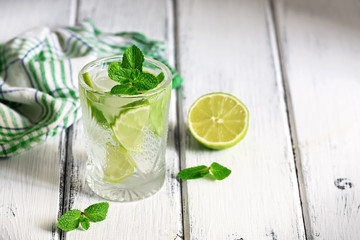 Refreshing cold drink with lime and mint in a glass on a white wooden board table. Traditional summer mojito cocktail. Selective focus, copy space