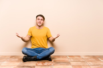 Young caucasian man sitting on the floor isolated showing a welcome expression.