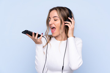 Young woman over isolated blue background listening music with a mobile and singing