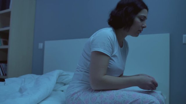 Depressed woman taking sedative pill before sleep sitting on bed alone, insomnia