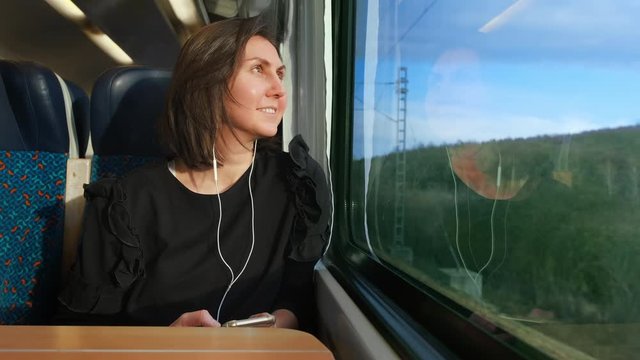 a young woman listens to a player and goes on a train in Europe. A woman looks out the window at nature and she likes to see
