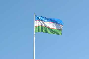 Uzbekistan flag on a flagpole against the blue cloudless sky