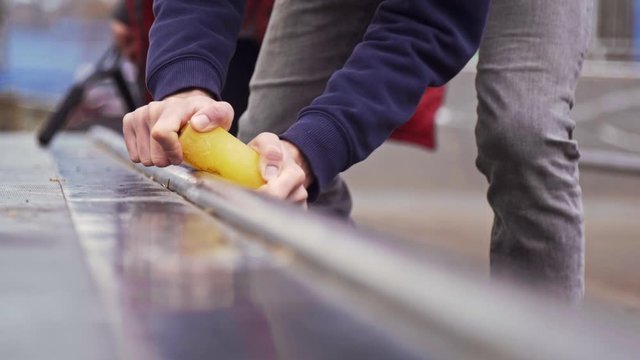 Aggressive skater applying wax on a box for sliding tricks at the skatepark