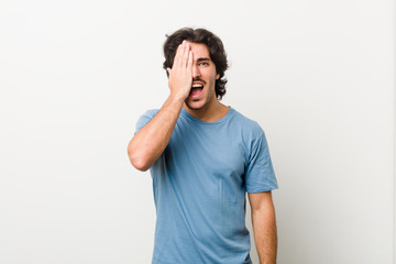 Young handsome man against a white background having fun covering half of face with palm.