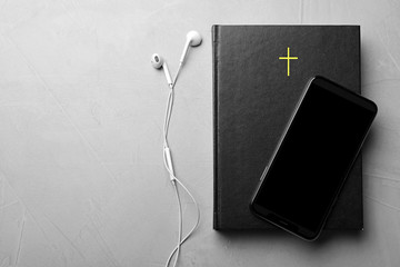 Bible, phone and earphones on light grey background, flat lay with space for text. Religious...