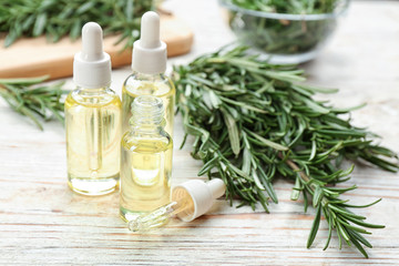 Bottles of rosemary essential oil on white wooden table