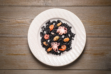 Delicious black risotto with seafood on wooden table, top view
