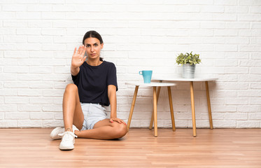 Young woman sitting on the floor making stop gesture with her hand