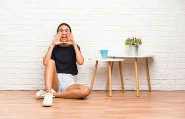 Young woman sitting on the floor shouting with mouth wide open