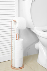 Holder with paper rolls near toilet bowl in bathroom