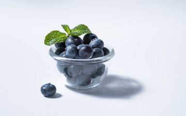 few  fresh blueberries in bowl with mint leaves on a white background