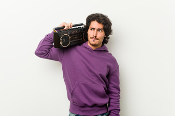 Young urban man holding a guetto blaster confused, feels doubtful and unsure.