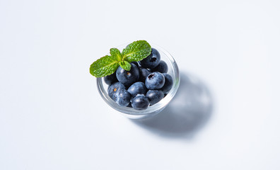 few  fresh blueberries in bowl with mint leaves on a white background