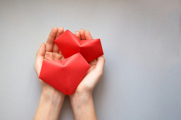Women's hands hold two red origami paper hearts made with their own hands on a light isolated background for Valentine's Day. Space for text.