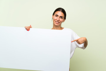 Young woman over isolated green background holding an empty white placard for insert a concept