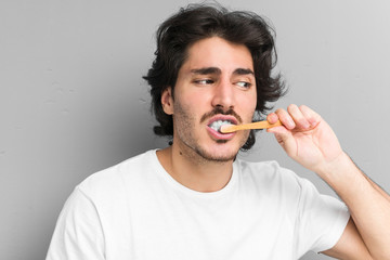 Young caucasian man cleaning his teeth with a toothbrush isolated in a grey background