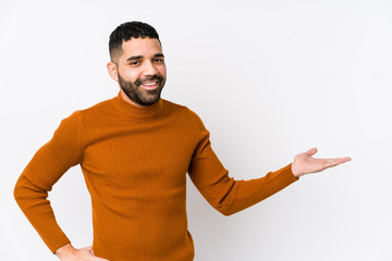 Young latin man against a white background isolated showing a copy space on a palm and holding another hand on waist.