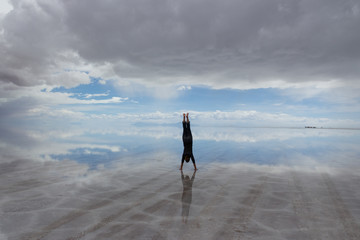Woman in handstand in centre of view of Salar De Uyuni Saltflats, Bolivia, with water reflecting...
