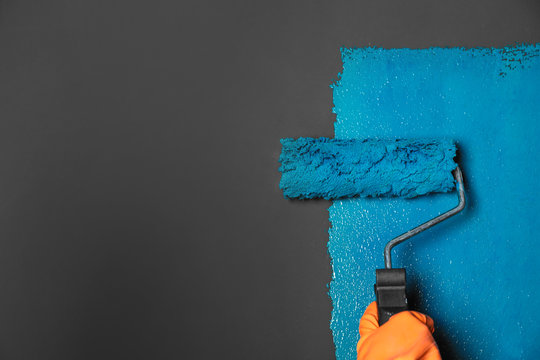 Woman painting grey wall with blue dye, closeup. Space for text