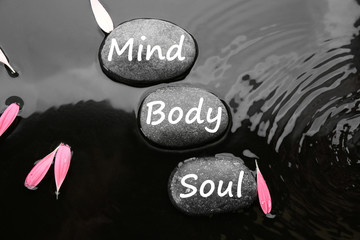 Spa stones with words Mind, Body, Soul and pink flower petals in water, flat lay. Zen lifestyle