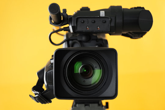 Modern professional video camera on yellow background, closeup