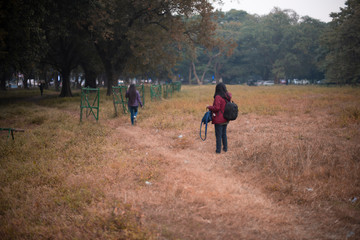 Obraz premium Back side of two young brunette Indian Bengali women/sisters with jackets and woolen sweater are walking in dry grass field in autumn afternoon in fall background. Indian lifestyle and fall.