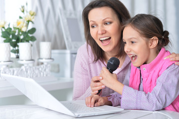 Fototapeta premium Portrait of emotional mother and daughter singing karaoke