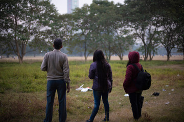 Fototapeta premium Back side of an Indian Bengali family in winter jacket and sweater enjoying an outing in a dry grass field in winter afternoon in natural background. Indian lifestyle and winter.