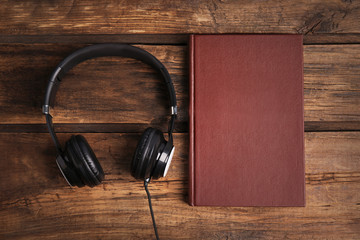 Book and modern headphones on wooden table, flat lay