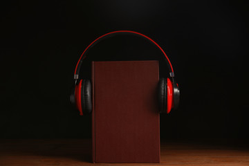 Headphones and book on wooden table against black background