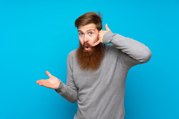 Redhead man with long beard over isolated blue background making phone gesture and doubting