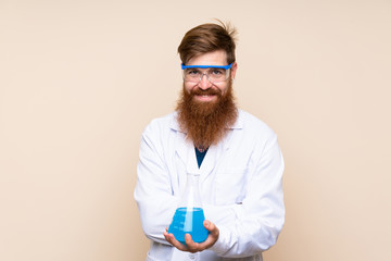 Redhead man with long beard over isolated background with a scientific test tube © luismolinero