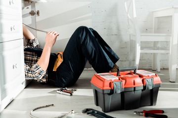 cropped view of installer lying on floor near tool box