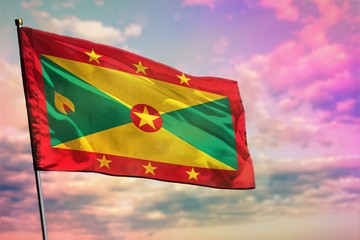Fluttering Grenada flag on colorful cloudy sky background. Prosperity concept.