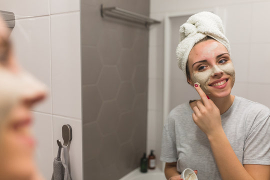 woman applying clay face mask in bathroom