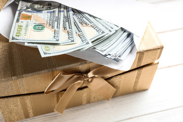 Gift box with dollar bills on white wooden table